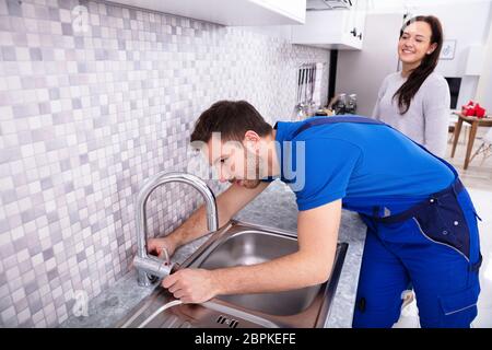 Donna felice Guardando idraulico maschio che fissa il rubinetto in cucina Foto Stock