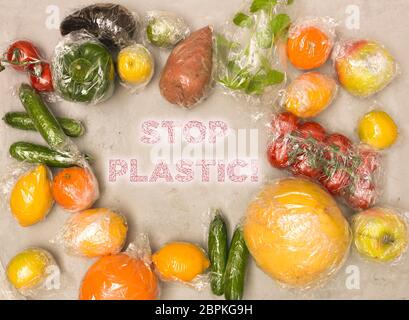 Molti diversi tipi di frutta e verdura sono avvolti in una pellicola di plastica, imballati su sfondo di calcestruzzo Foto Stock