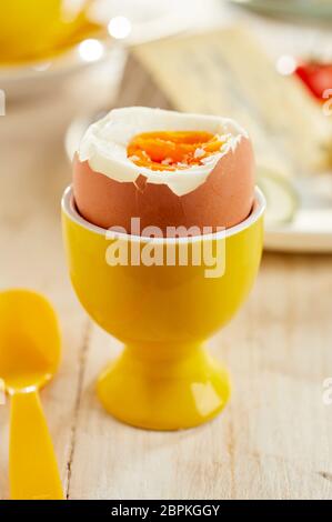 Soft-uova sode o serviti in ceramica di colore giallo eggcup sul tavolo di legno con cucchiaio in plastica Foto Stock