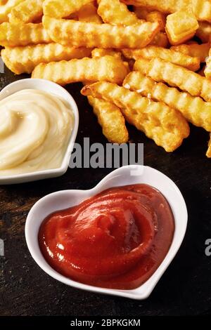 A forma di cuore ciotole di ketchup o salsa di pomodoro e maionese cremosa serviti come accompagnamento al croccante di golden crinkle cut potato chips o Pommes Fri Foto Stock