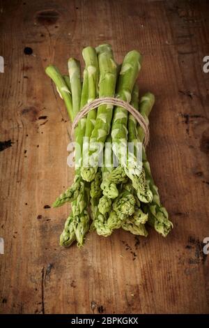 Bundle di fresco verde i turioni degli asparagi legati con spago su una tavola in legno rustico visto elevato angolo con copia spazio e vignette Foto Stock