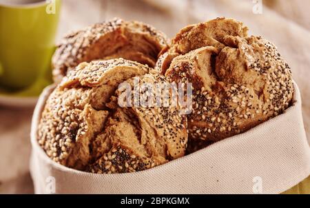 Di panini freschi di forno croccante pane integrale con crosta incrinato e rabboccato con semi, servita nel sacco di tessuto con tazza di bevanda in background. Close-up v Foto Stock