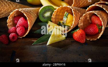 Set di frutta fresca e bacche dessert in cialda coni scuri in legno laccato in superficie, visto da vicino Foto Stock