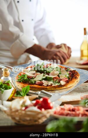 Lo Chef condimento di una pizza guarnita con rucola formaggio e salsa di pomodoro in una pizzeria in una stretta fino alle mani Foto Stock