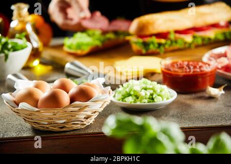 Cesto in Vimini Di uova fresche su un bancone cucina con verdure fresche e gli ingredienti per i panini da asporto in un ristorante Foto Stock