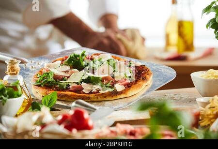 Pizzeria in metallo con pagaia crusty pizza italiana e rabboccato con rucola e prosciutto e formaggio con ingredienti in primo piano Foto Stock