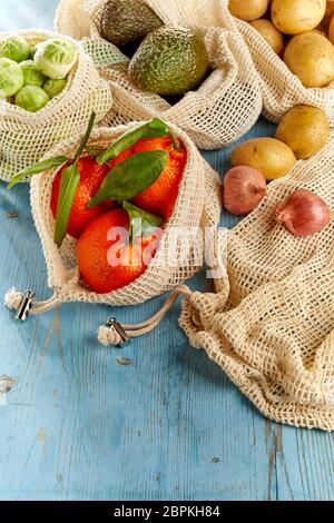 Assortimento di negozi di generi alimentari organici riutilizzabili in eco-friendly net sacchetti. Arance fresche, avocadi, i cavoli di Bruxelles, patate e cipolla blu sul tavolo di legno, Foto Stock