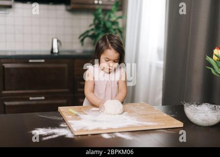 Carina bella bambina prepara l'impasto per cuocere i biscotti al tavolo Foto Stock