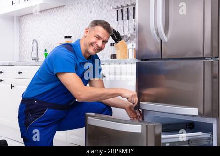 Maschio maturo del veterano della riparazione di un frigorifero con Toolbox in cucina Foto Stock