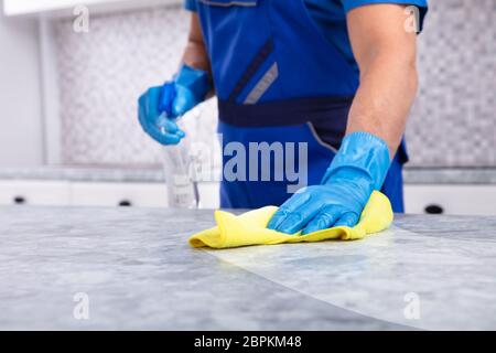 La sezione centrale di un maschio bidello sporca la pulizia della cucina con la bottiglia spray e igienico Foto Stock