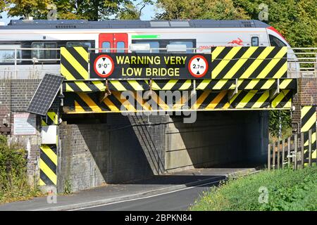 Maggiore Anglia passeggero treno parte Ely stazione ferroviaria traversata bassa ponte stradale di contrassegni di pericolo I simboli di avvertenza e firmare Cambridgeshire England Regno Unito Foto Stock