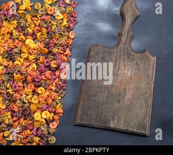 Vecchio vuoto tagliere di legno e impreparati fusilli spirale multicolore di farina di frumento Foto Stock