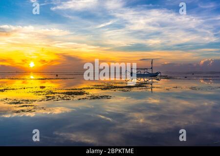 Un indonesiano barca da pesca di sunrise, riflessi nell'acqua, Sanur, Bali, Indonesia, 21 aprile 2018 Foto Stock