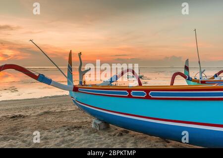 Un'alba colorata con una tradizionale barca da pesca indonesiana, riflessi in acqua, Sanur, Bali, Indonesia, 21 aprile 2018 Foto Stock