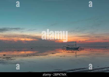 Imbarcazione da pesca indonesiana al crepuscolo, vicino alla riva, riflessi rossi in acqua, Sanur, Bali, Indonesia, 21 aprile 2018 Foto Stock