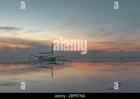 Una piccola barca indonesiana da pesca all'alba, riflessi in acqua, Sanur, Bali, Indonesia, 21 aprile 2018 Foto Stock