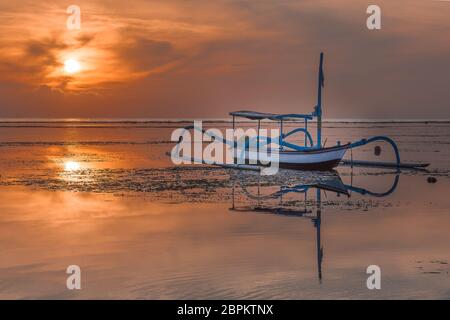 Un indonesiano barca da pesca di sunrise, riflessi nell'acqua, Sanur, Bali, Indonesia, 21 aprile 2018 Foto Stock