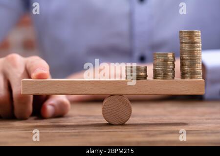 Imprenditore di bilanciamento delle monete impilate con il dito sull'altalena in legno Foto Stock