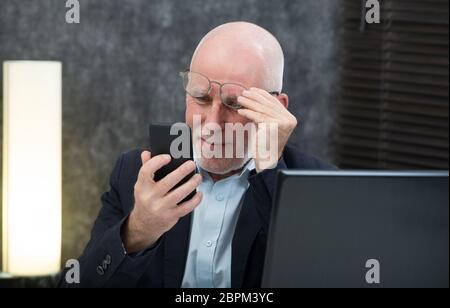 Un imprenditore senior utilizzando lo smartphone, egli sta avendo difficoltà e problemi di visione Foto Stock