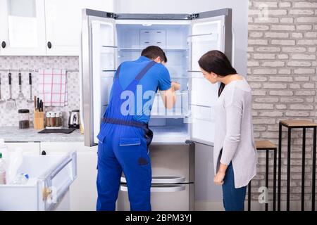 Donna che guarda la voce maschile Repairman frigorifero di fissaggio con un cacciavite Foto Stock