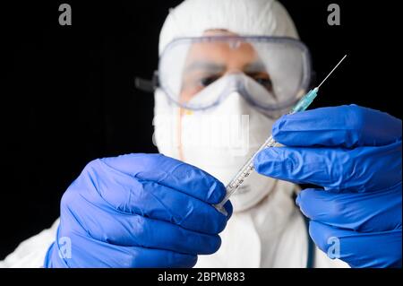 Medico o scienziato in DPI suite uniforme in laboratorio tenere liquido vaccino flacone e siringa su fondo nero isolato . Foto Stock