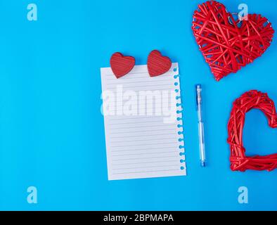 In vimini in legno cuore rosso e un vuoto di foglio bianco di notepad, sfondo blu Foto Stock