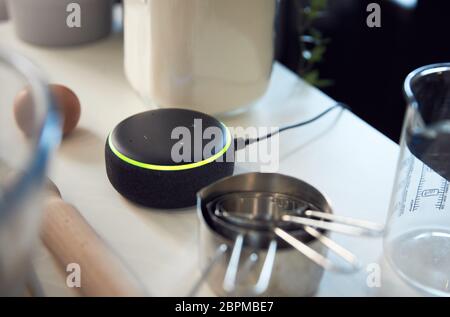 Altoparlante Home intelligente che risponde a Donna in cucina a casa mentre si cuoce in blocco Foto Stock