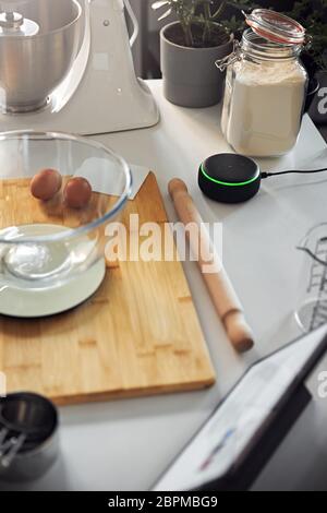 Altoparlante Home intelligente che risponde a Donna in cucina a casa mentre si cuoce in blocco Foto Stock