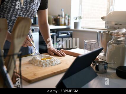 Persona anonima che fa la pasta fresca a casa nella cucina, guardando UNA ricetta video con le uova e la farina. Foto Stock