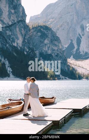 Gli sposi camminano lungo un molo di legno al Lago di Braies in Italia. Matrimonio in Europa, sul lago Braies. Gli sposi novelli camminano, baciano, abbracciano su un Foto Stock