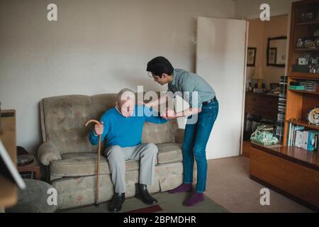 Ragazzo adolescente sta aiutando il nonno di alzarsi dal divano nel salotto di casa sua. Foto Stock