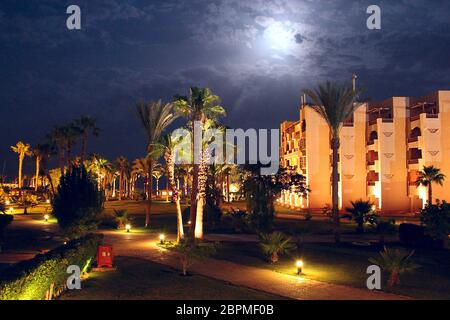 Moonlight, un luminoso resort tropicale con un edificio alberghiero e palme di notte. Resort notturno con bei pedoni e erba tra palme Foto Stock