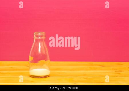 Un terzo di pinta di vetro bottiglia di latte con la feccia della banana frullato, su di un tavolo di legno contro una rosa di sfondo dipinto Foto Stock