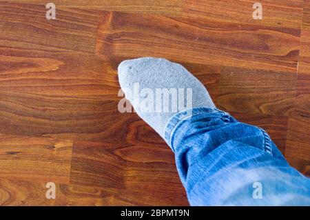 Gambe di un uomo in jeans blu con calze grigie su un pavimento di legno Foto Stock