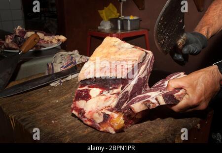 Macellaio. Carne di Chianina. Tagliare con un coltello. Un uomo viene tagliato con un coltello soffia un grosso pezzo di carne italiana. Chianina origine fiorentina Foto Stock