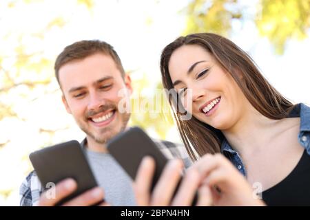 Ritratto di una coppia felice utilizzando i loro telefoni intelligenti a camminare in un parco Foto Stock