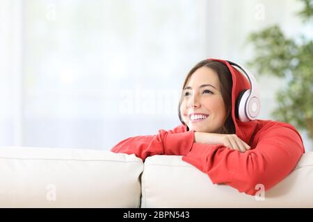 Dreamer girl teen ascolto di musica con cuffie su un divano nel soggiorno di casa e guardando al di sopra con lo spazio di copia Foto Stock