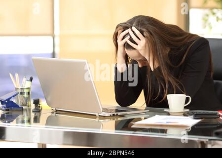 Imprenditrice disperata sulla linea preoccupato dopo il fallimento di fronte a un computer portatile con le sue mani in testa in ufficio Foto Stock