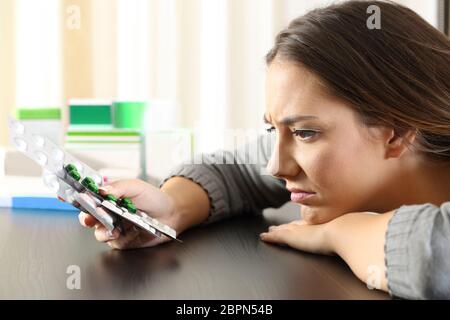 Vista laterale di una donna dubbia che tiene un sacco di farmaci su un tavolo a casa Foto Stock