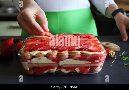 Concetto di dessert tiramisù. Dessert italiano fatto in casa. Donna che decorano a mano il tiramisù con fette di fragole fresche. Primo piano. Foto Stock