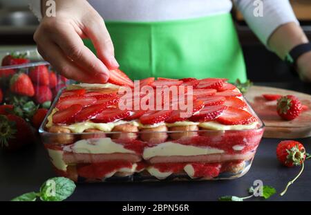 Concetto di dessert tiramisù. Dessert italiano fatto in casa. Donna che decorano a mano il tiramisù con fette di fragole fresche. Primo piano. Foto Stock