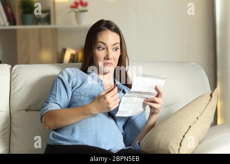 Diffidenti donna incinta la lettura di un foglio illustrativo prima di prendere una pillola seduta su un divano nel salotto di casa Foto Stock