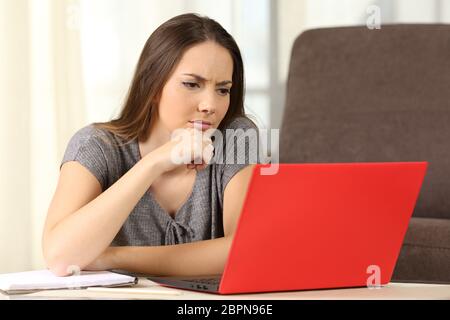Malinconici studente on line con un computer portatile rossa seduta sul pavimento nel salotto di casa Foto Stock