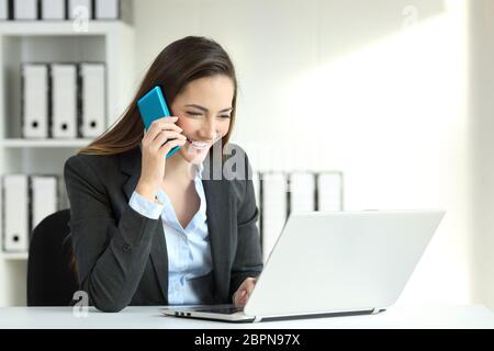 Lavoratore di ufficio a parlare su una chiamata di telefono e i dati di controllo in un computer portatile Foto Stock