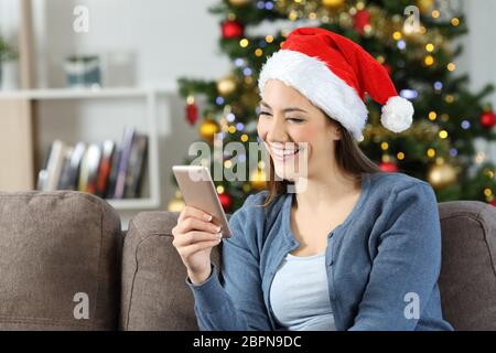 Lettura della ragazza messaggi telefonici in natale seduto su un divano nel salotto di casa Foto Stock