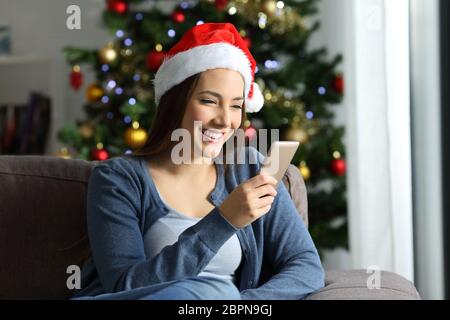 Donna felice controllo messaggi telefonici in natale seduto su un divano nel salotto di casa Foto Stock