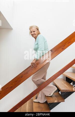 Donna anziana a casa usando un bastone da passeggio per scendere le scale Foto Stock