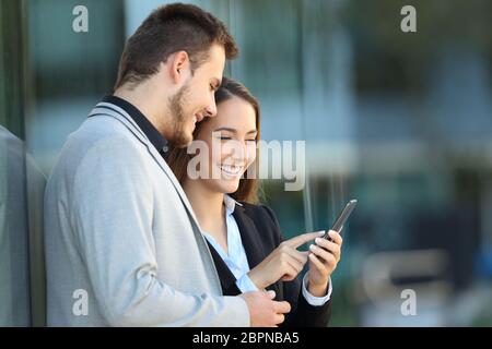 Due dirigenti che utilizzano un telefono cellulare appoggiati su un edificio aziendale in strada Foto Stock