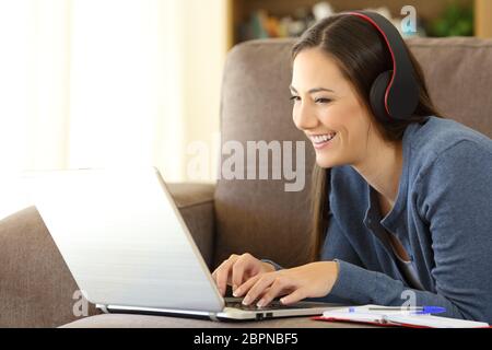 Ritratto di un felice apprendimento dello studente on line guardando e ascoltando i tutorial in un laptop che giace su un divano a casa Foto Stock