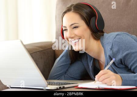 Ragazza felice apprendimento in linea audio ascolto tutorial con le cuffie e un laptop sdraiato su un lettino a casa Foto Stock